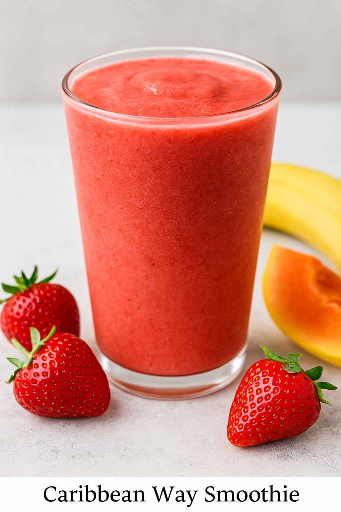 Caribbean Way smoothie in a clear glass surrounded by strawberries, banana, papaya slice.